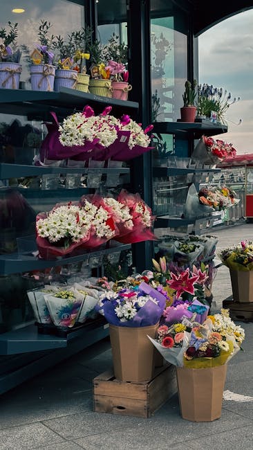 An outdoor floral display at floristleabridge.co.uk featuring a variety of fresh flowers arranged in colorful bouquets and potted plants. The display includes white hyacinths and pink lilies wrapped i