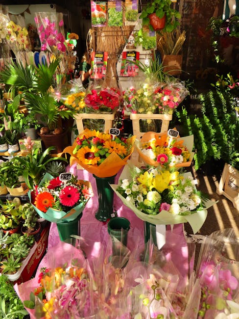 A vibrant display of fresh flower bouquets arranged on a pink table within a flower shop. The bouquets feature a variety of colourful blooms, including bright yellow sunflowers, pink gerbera daisies,
